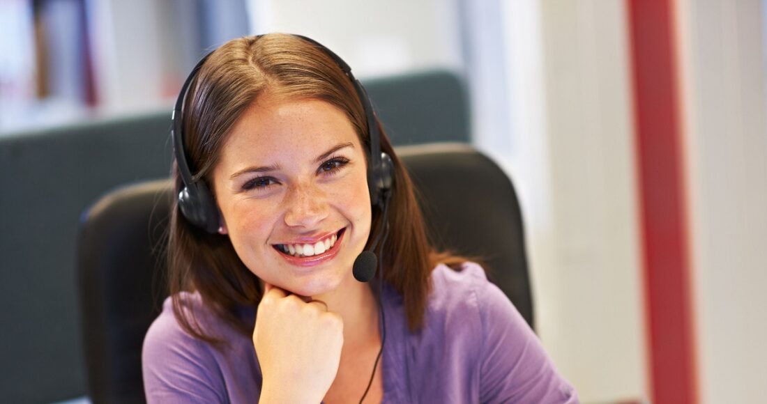 Customer service representative wearing a headset, smiling at the desk.