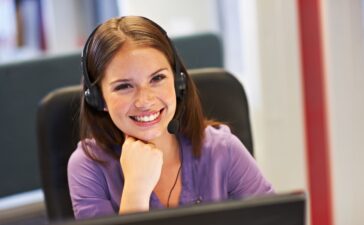 Customer service representative wearing a headset, smiling at the desk.